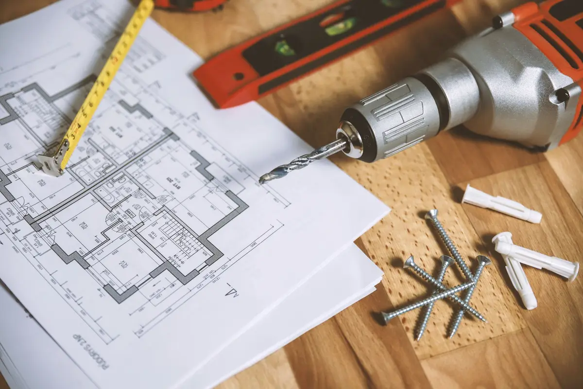 Plano de una vivienda sobre la mesa junto a un taladro y tornillos
